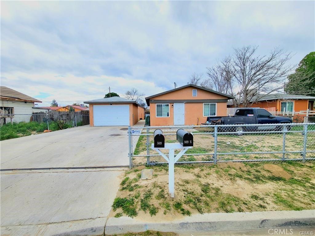 ranch-style home with a fenced front yard, an outbuilding, driveway, and stucco siding