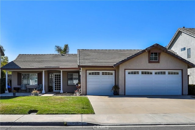 view of front of property featuring driveway, a tile roof, an attached garage, a front lawn, and stucco siding