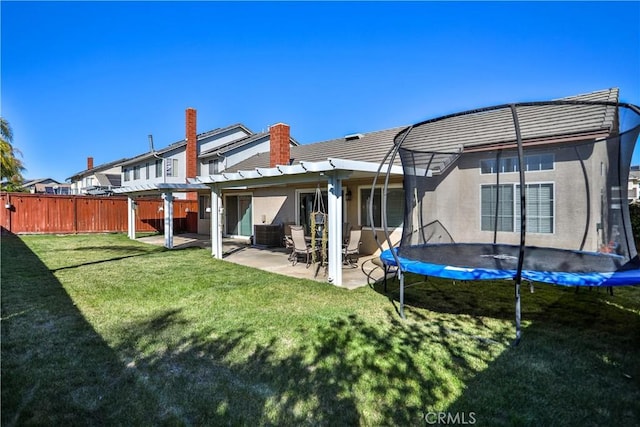 rear view of house featuring fence, a yard, stucco siding, a trampoline, and a patio area