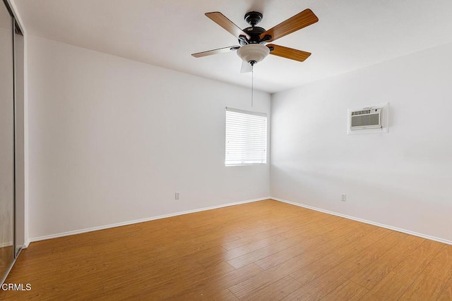 empty room featuring light wood-type flooring, a wall unit AC, a ceiling fan, and baseboards