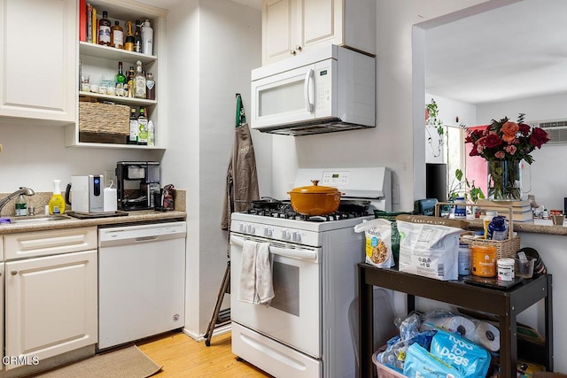 kitchen with white appliances, light wood finished floors, light countertops, white cabinetry, and a sink