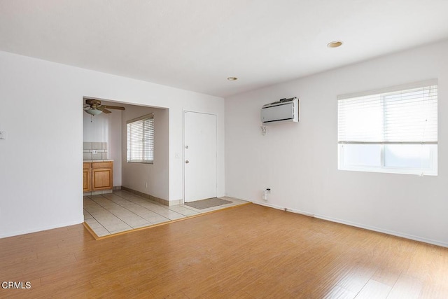 unfurnished room with baseboards, light wood-type flooring, a ceiling fan, and a wall mounted air conditioner