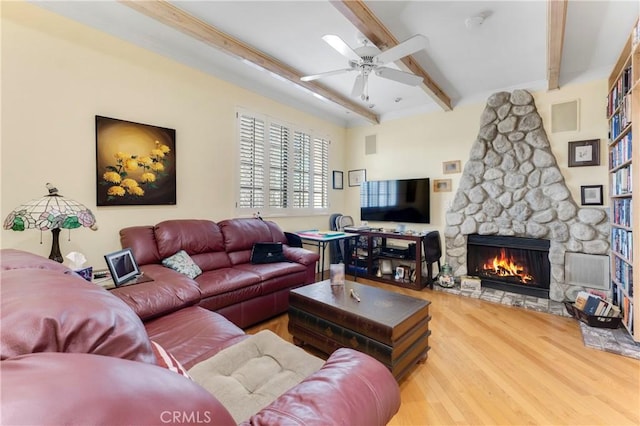 living room with ceiling fan, beamed ceiling, a stone fireplace, and wood finished floors