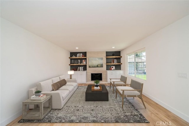 living room with built in features, a large fireplace, light wood-style flooring, and baseboards