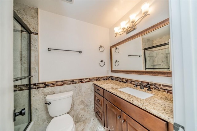 bathroom featuring a wainscoted wall, a notable chandelier, tile walls, toilet, and vanity