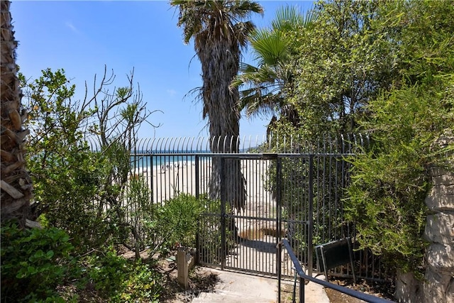 view of gate with a water view, fence, and a beach view