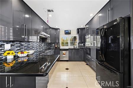 kitchen featuring wall oven, light tile patterned floors, modern cabinets, freestanding refrigerator, and under cabinet range hood