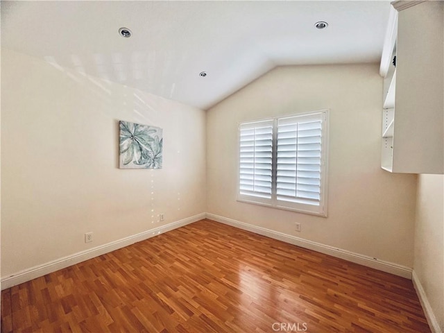 empty room featuring vaulted ceiling, wood finished floors, and baseboards