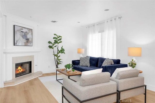 living room featuring a warm lit fireplace, wood finished floors, and visible vents