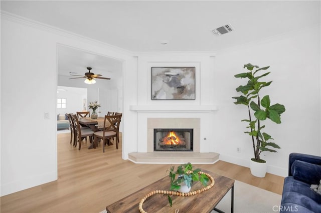 living room with a warm lit fireplace, visible vents, wood finished floors, and ornamental molding