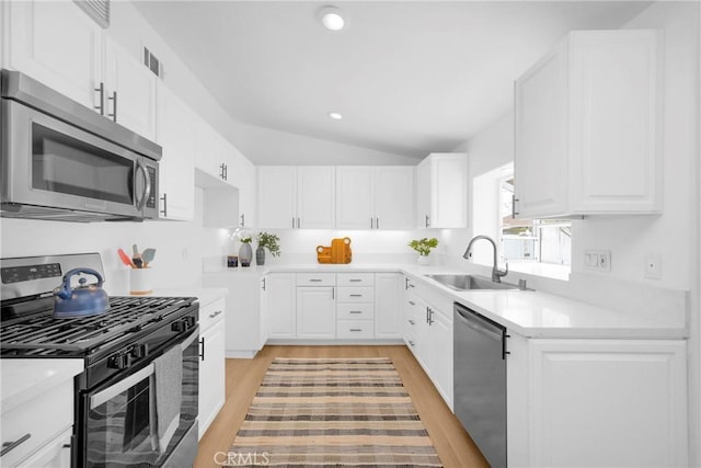 kitchen with appliances with stainless steel finishes, vaulted ceiling, white cabinets, and a sink