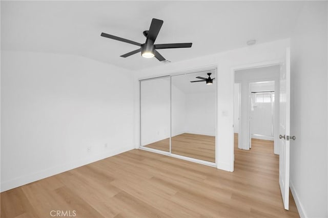 unfurnished bedroom featuring baseboards, a closet, a ceiling fan, and light wood-style floors