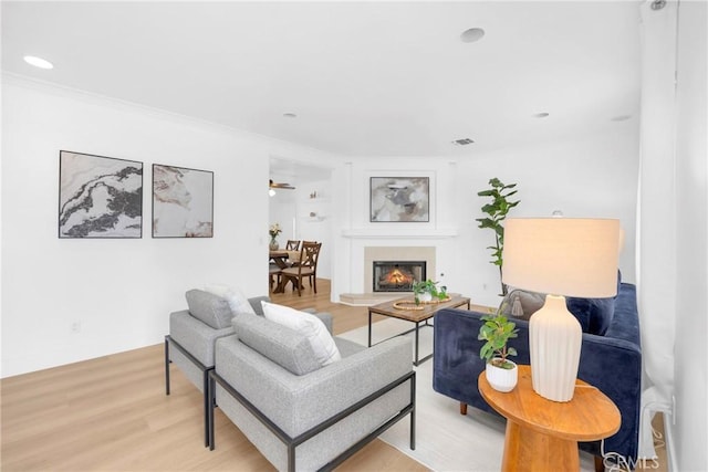 living area with light wood finished floors, visible vents, a glass covered fireplace, crown molding, and recessed lighting