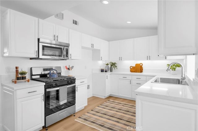 kitchen with stainless steel appliances, a sink, visible vents, light wood-style floors, and white cabinets