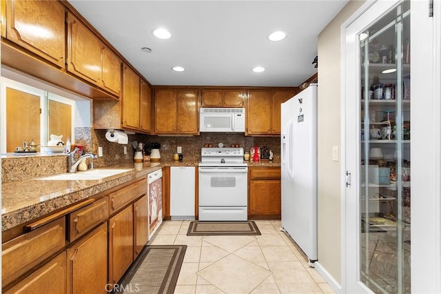 kitchen featuring brown cabinets, light tile patterned floors, tasteful backsplash, a sink, and white appliances