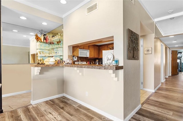 kitchen featuring light wood-type flooring, white microwave, visible vents, and a breakfast bar area