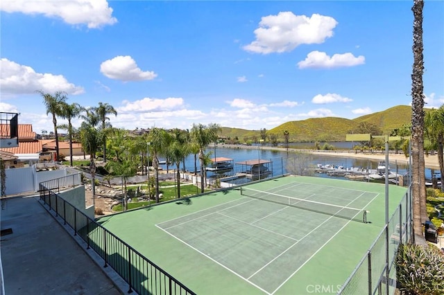 view of tennis court featuring fence and a water and mountain view