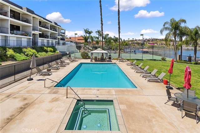 community pool with a patio area, fence, and a hot tub