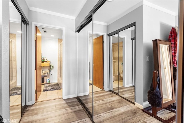 hallway with light wood-type flooring, crown molding, and baseboards