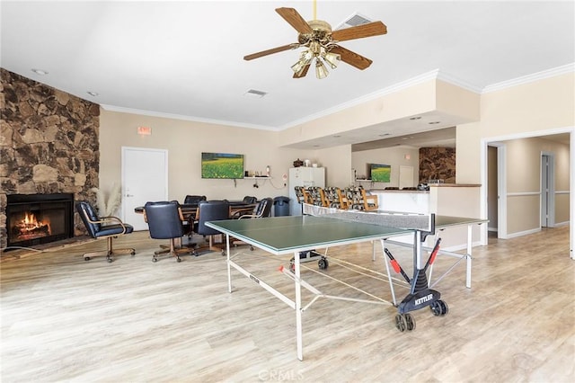 rec room featuring visible vents, ornamental molding, ceiling fan, a stone fireplace, and wood finished floors