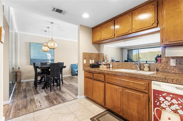 kitchen featuring white dishwasher, visible vents, brown cabinetry, and a sink