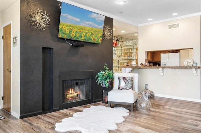 living area with recessed lighting, wood finished floors, visible vents, baseboards, and a lit fireplace