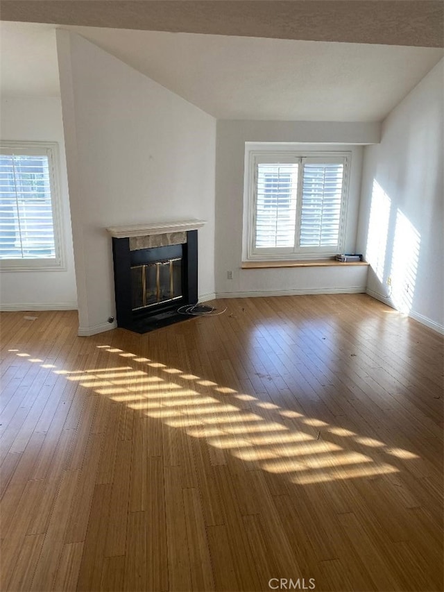 unfurnished living room featuring vaulted ceiling, a fireplace with flush hearth, and hardwood / wood-style flooring