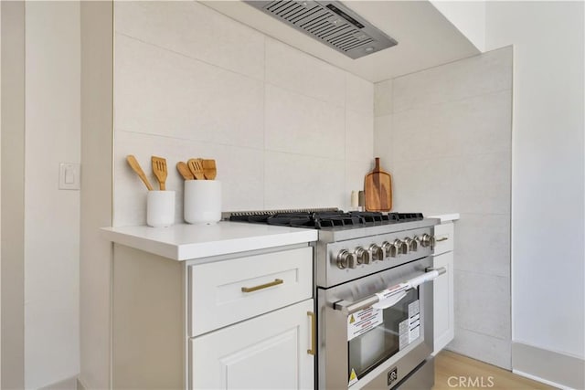 kitchen with range hood, stainless steel range, tile walls, light countertops, and white cabinetry