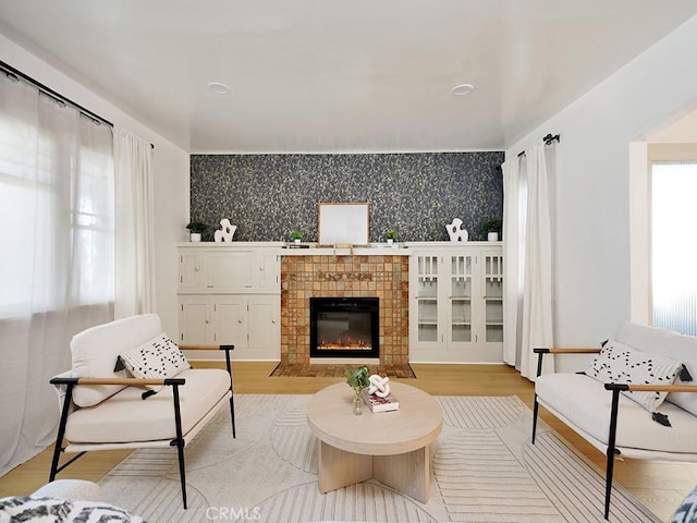 living area featuring wallpapered walls, a fireplace, an accent wall, and light wood-style floors