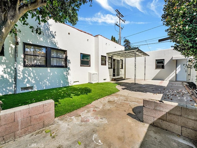 rear view of house with a yard, a pergola, a patio area, and stucco siding