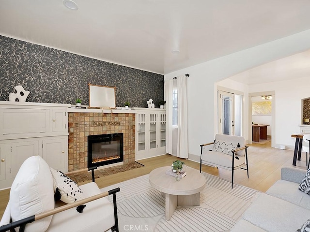 living area featuring wallpapered walls, baseboards, a fireplace with flush hearth, an accent wall, and light wood-type flooring