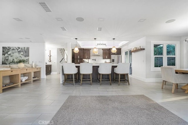 kitchen featuring stainless steel fridge with ice dispenser, light countertops, visible vents, wall chimney range hood, and a kitchen bar