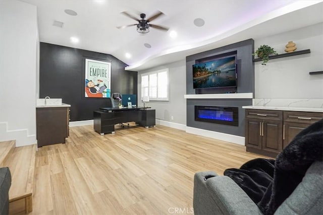 living room with a glass covered fireplace, baseboards, ceiling fan, and light wood finished floors