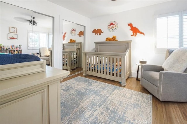 bedroom featuring a nursery area, baseboards, and wood finished floors