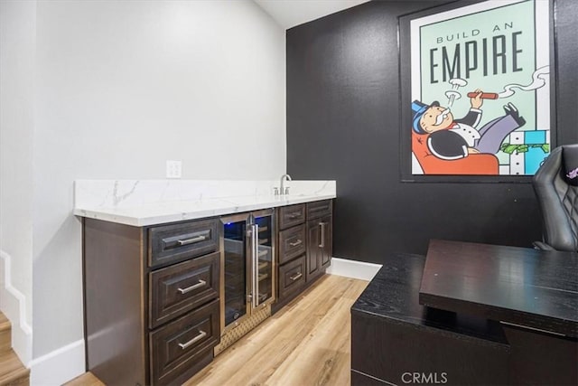 bar with beverage cooler, light wood finished floors, indoor wet bar, and baseboards