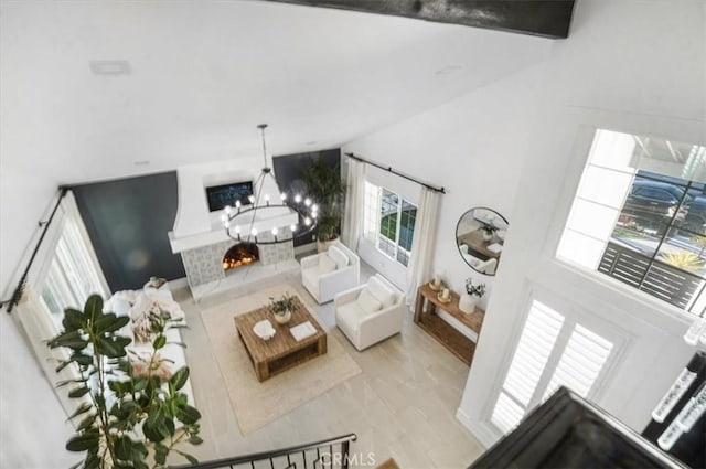 living room with a warm lit fireplace, a notable chandelier, and vaulted ceiling