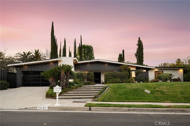 mid-century modern home with a garage, concrete driveway, and a lawn