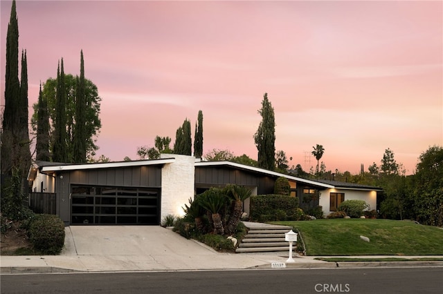 mid-century inspired home featuring a garage, board and batten siding, driveway, and a lawn