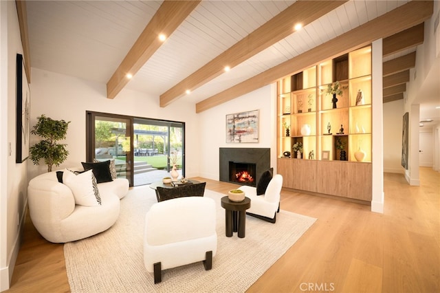 living room with light wood-style floors, a warm lit fireplace, lofted ceiling with beams, and baseboards