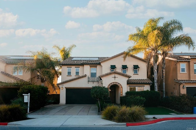 mediterranean / spanish-style house featuring an attached garage, a tile roof, concrete driveway, roof mounted solar panels, and stucco siding