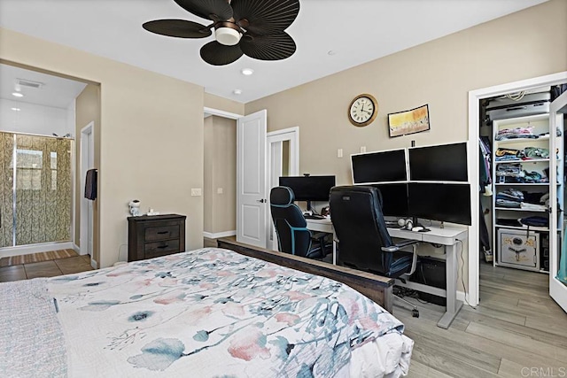 bedroom featuring a walk in closet, light wood finished floors, ensuite bathroom, a ceiling fan, and baseboards