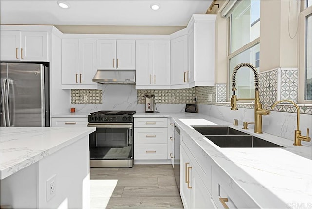 kitchen featuring appliances with stainless steel finishes, light stone countertops, under cabinet range hood, white cabinetry, and a sink