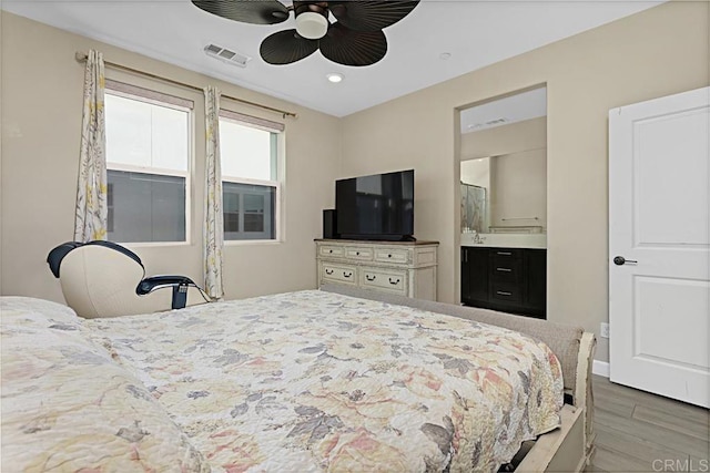 bedroom with ensuite bath, wood finished floors, visible vents, and a ceiling fan