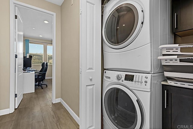 clothes washing area featuring baseboards, laundry area, wood finished floors, and stacked washer / drying machine