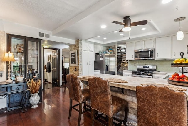 kitchen with stainless steel appliances, a raised ceiling, visible vents, and dark wood-style floors