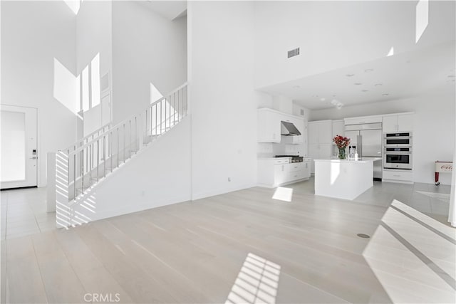 living area featuring light wood-style flooring, a high ceiling, visible vents, baseboards, and stairway