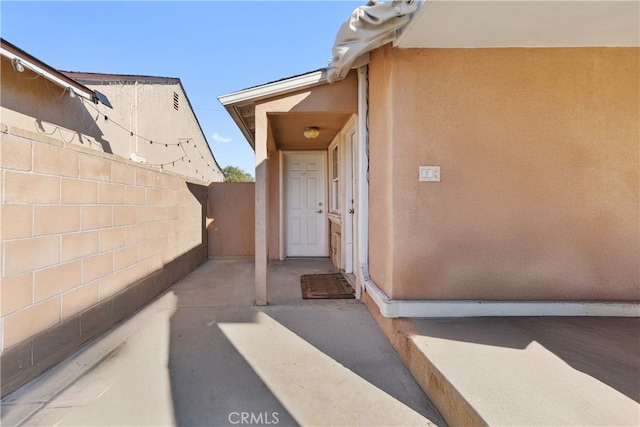 doorway to property with a patio area, fence, and stucco siding