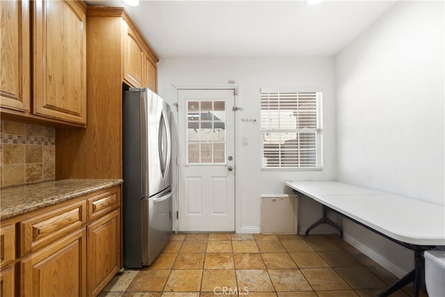 kitchen with stone tile floors, baseboards, decorative backsplash, brown cabinets, and freestanding refrigerator