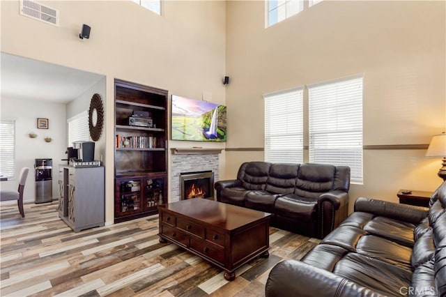 living area featuring a high ceiling, visible vents, a fireplace, and light wood finished floors