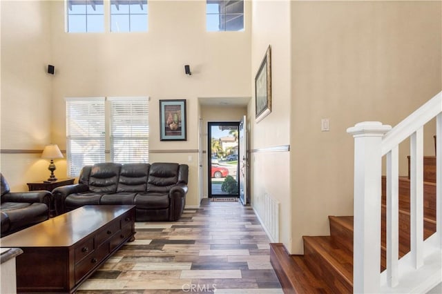 living area with a towering ceiling, light wood-style flooring, and stairway